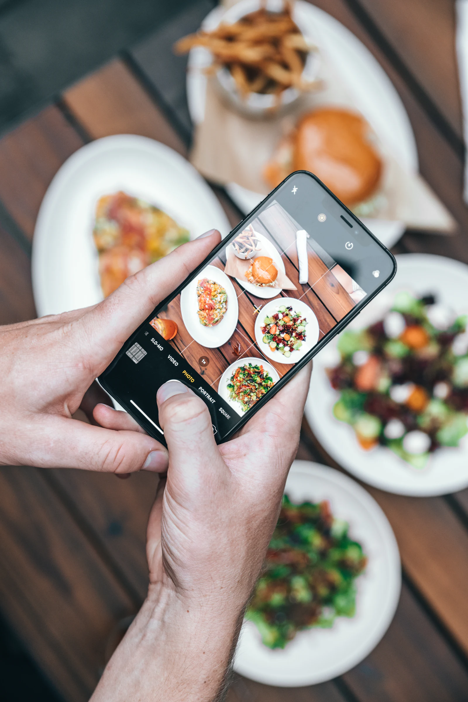 A hand holding a smartphone, framing plated dishes on a restaurant table to capture a menu-grade photo