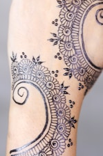 A detailed henna design featuring intricate floral and spiral patterns with delicate dot accents, applied to the skin. The artwork appears precise and ornate, showcasing traditional elements commonly used in henna art.