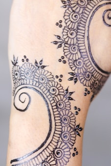 A detailed henna design featuring intricate floral and spiral patterns with delicate dot accents, applied to the skin. The artwork appears precise and ornate, showcasing traditional elements commonly used in henna art.