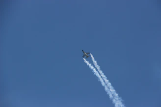 A sleek airplane soaring above clouds with a glowing cyan trail.