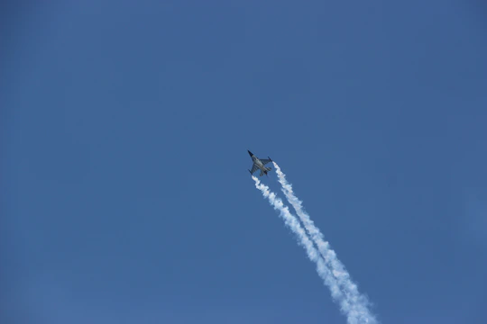 A sleek airplane soaring above clouds with a glowing cyan trail.