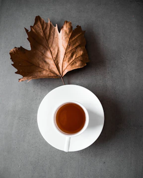 A steaming cup of black tea on a saucer with loose leaves beside it