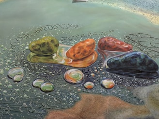 An artistic rendering of colorful stones resting on a surface, surrounded by swirling patterns and bubbles that resemble water. The stones vary in color, including green, orange, red, and blue hues. The background features intricate designs that enhance the impressionistic style of the artwork.