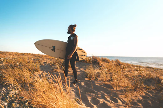 Someone carrying a surfboard down to the shore
