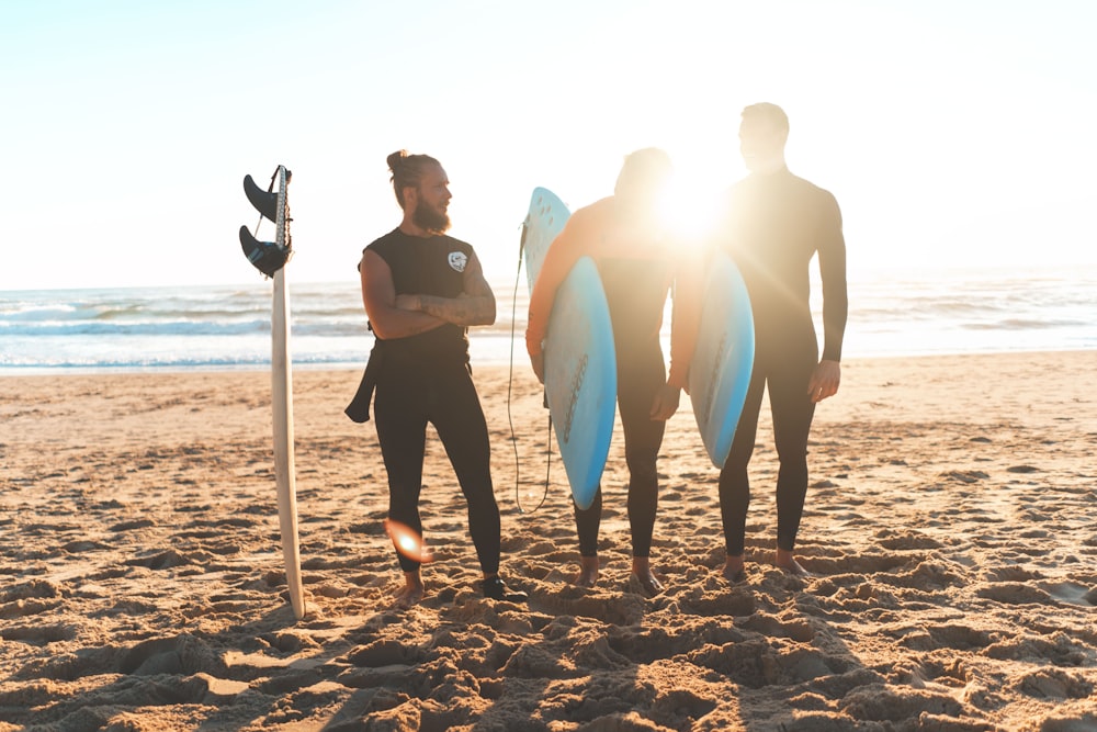 three men carrying surfboards standing on shore
