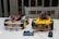 Two small wheeled robotic platforms with chassis and colorful wiring are placed on a table. Each robot features a yellow base with black tires and exposed circuit components. Nearby, a blue and black electronic board is connected with a wire.