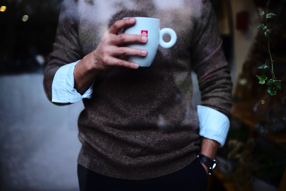 man in grey sweater holding blue ceramic mug