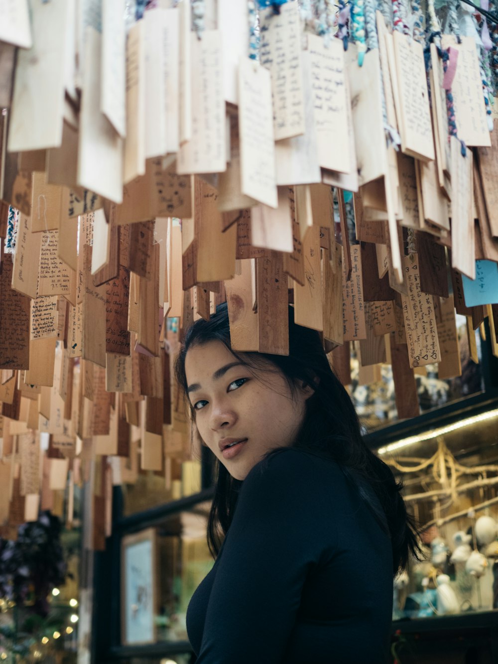 woman in dark blue long-sleeved top standing below hanging wood cards