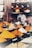 A variety of colorful spices are displayed in conical piles on a market stall, each labeled with small black signs. In the background, large jars filled with different substances are neatly arranged on shelves.