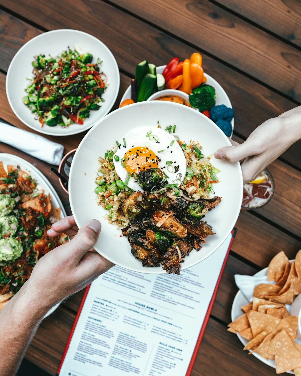 two hands holding white plate with foods