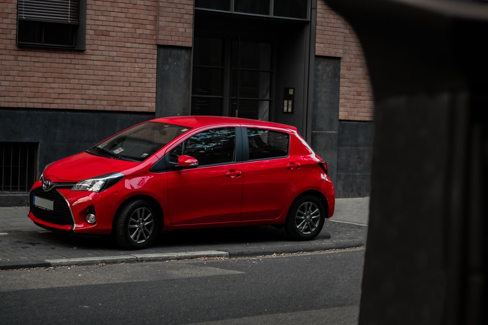 parked red 5-door hatchback beside building