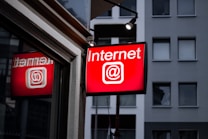 A brightly lit red sign displays the word 'Internet' with the @ symbol, mounted outside a building with a modern facade and several windows.