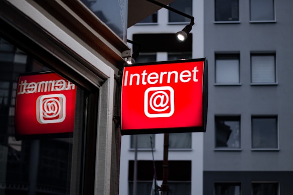 A brightly lit red sign displays the word 'Internet' with the @ symbol, mounted outside a building with a modern facade and several windows.