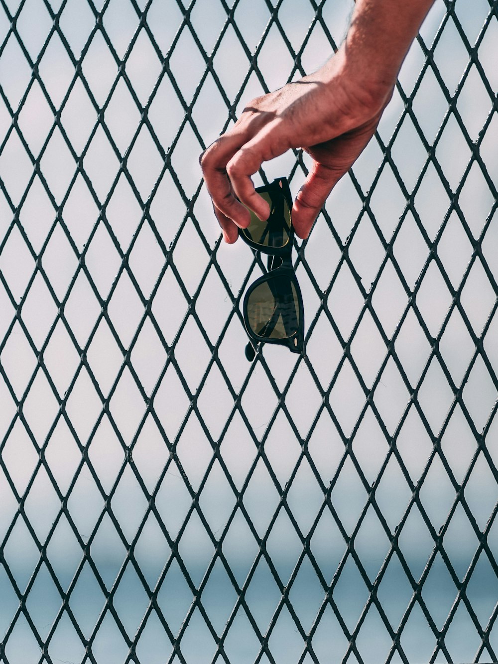 person touching black sunglasses on chain link fence