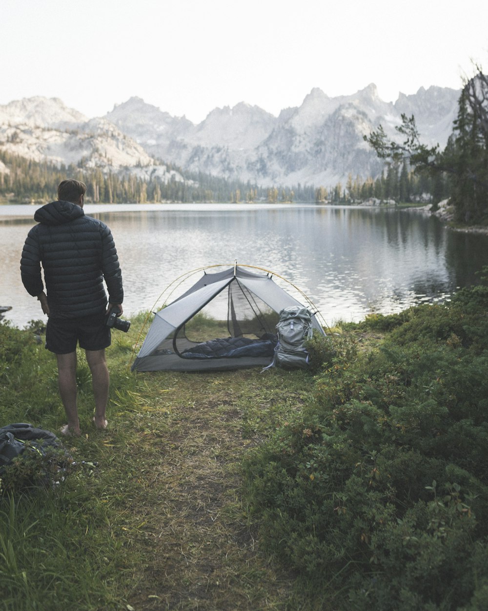 man standing beside tent near lake during day