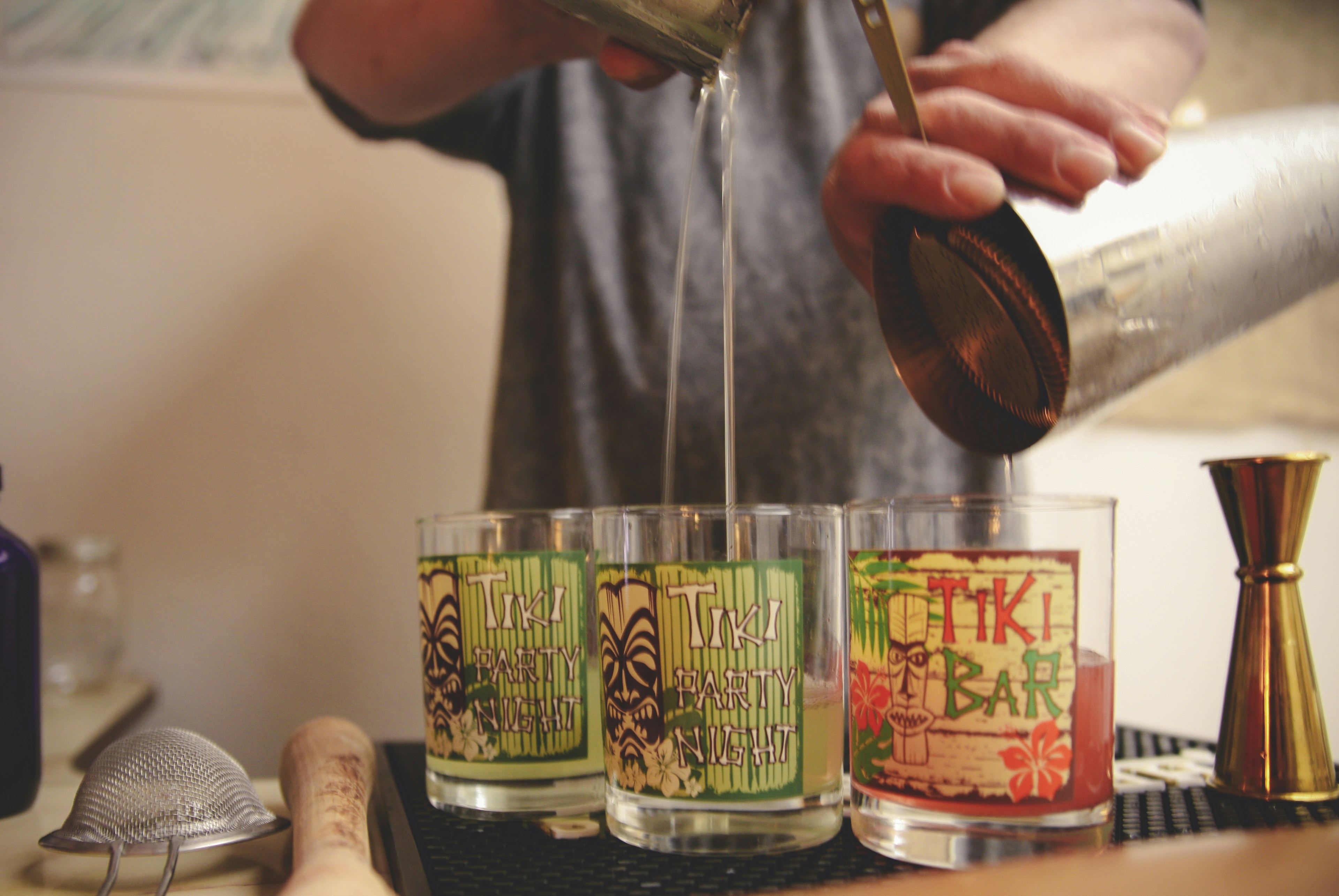 person pouring beverages in three Tiki glasses