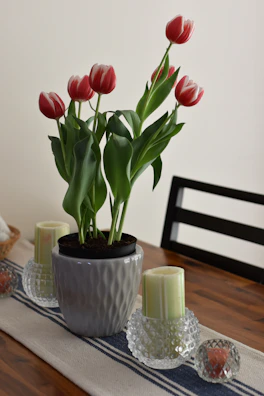 Brightly colored artificial tulips in a modern white pot on a wooden table.
