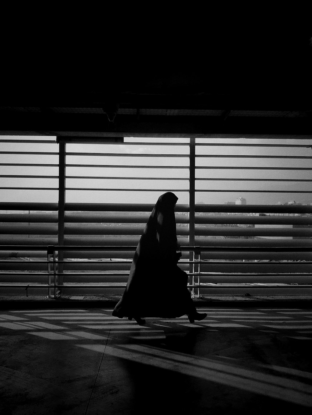 Foto en escala de grises de una mujer caminando cerca de la ventana