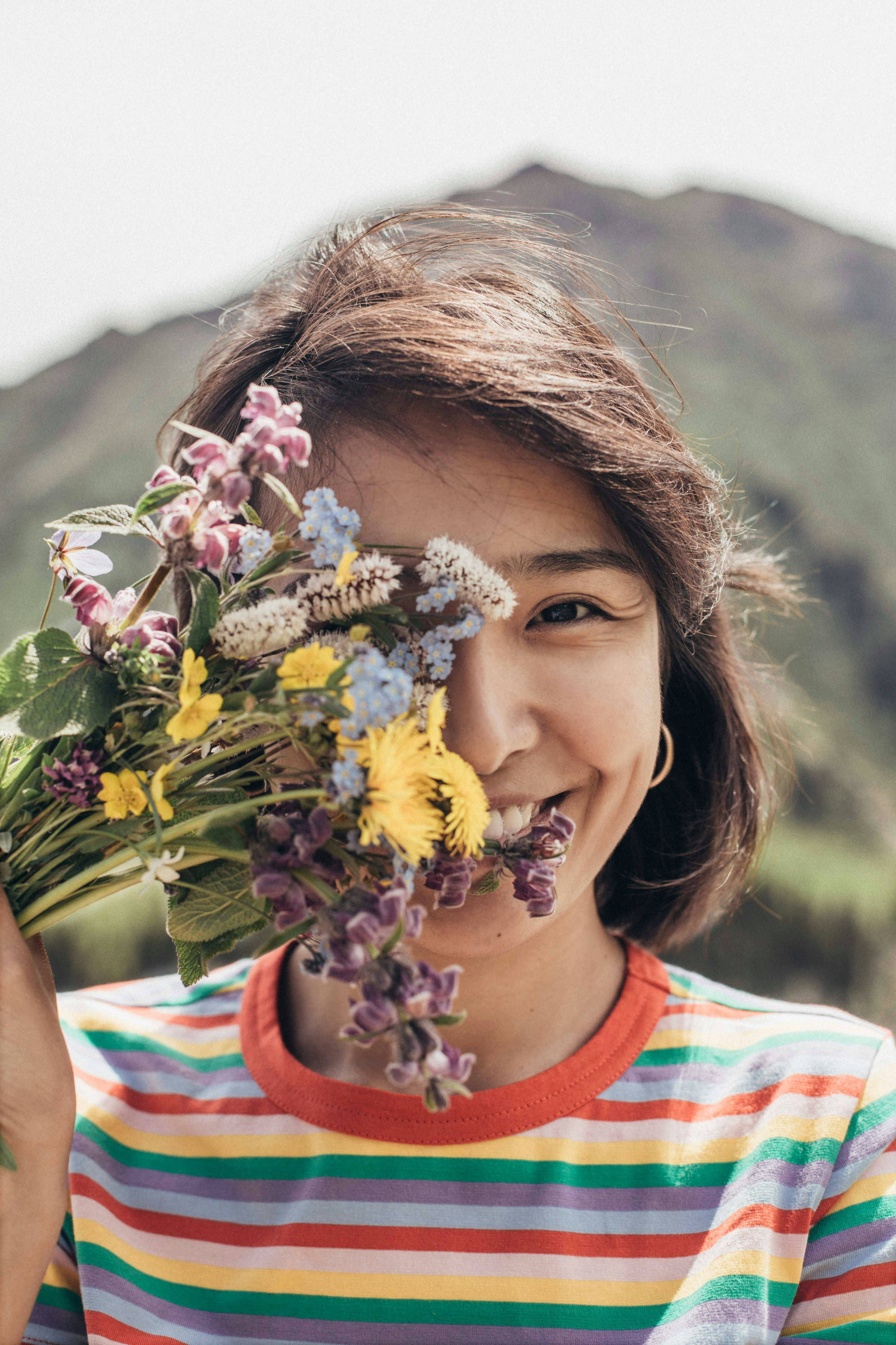 girl standing and covering her right eye with petaled flowers and smiling