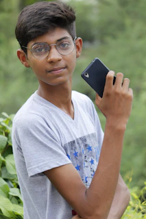 A young person happily using a basic mobile phone outdoors with a clear blue sky.