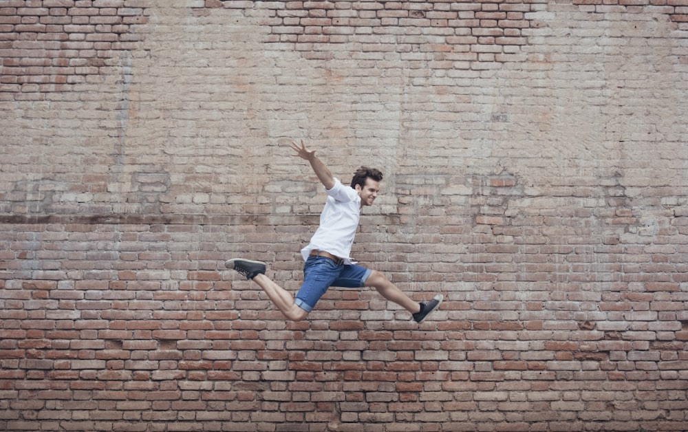 person in white shirt and blue denim jeans jumping beside brown walll