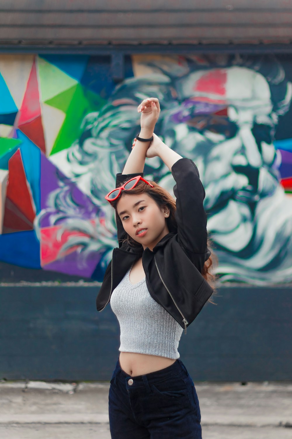 woman standing raising both her arms in front of wall with mural