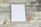 A blank framed canvas is surrounded by scattered wine corks on a rustic wooden surface. The scene has a vintage and artistic vibe, with corks placed randomly around the frame, suggesting a casual, creative atmosphere.