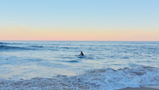 Sunrise over Taghazout beach with gentle waves and a lone surfer preparing to paddle out.