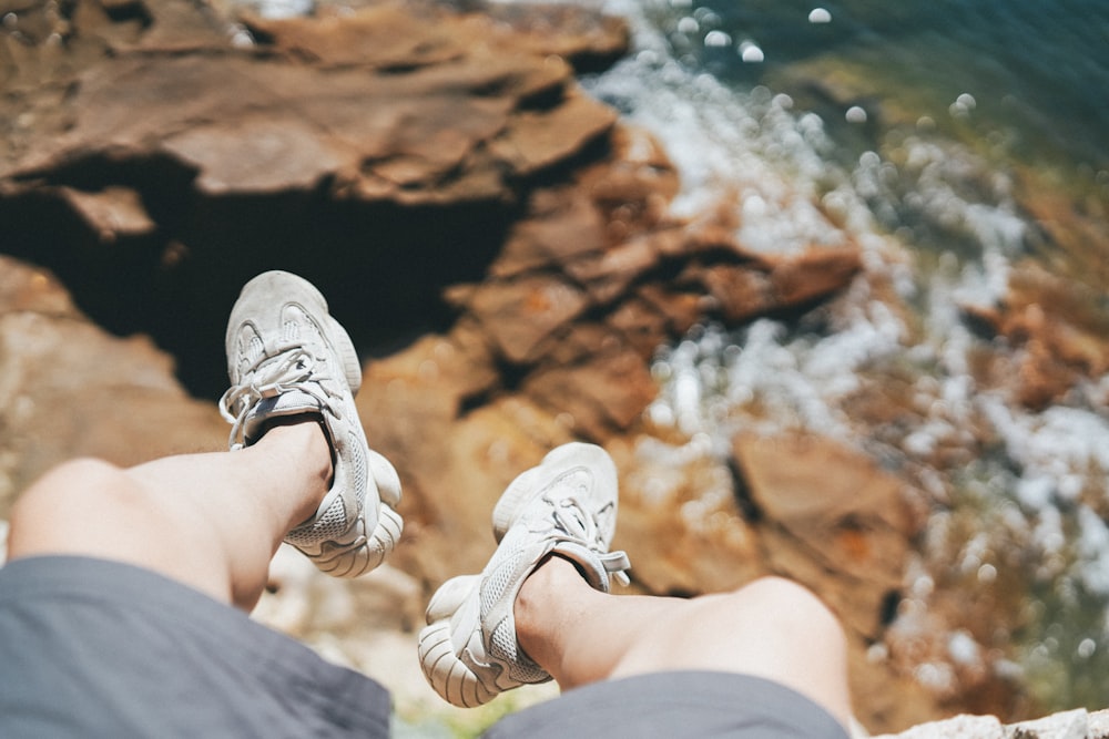 person in grey shorts and grey low-top sneakers on cliff