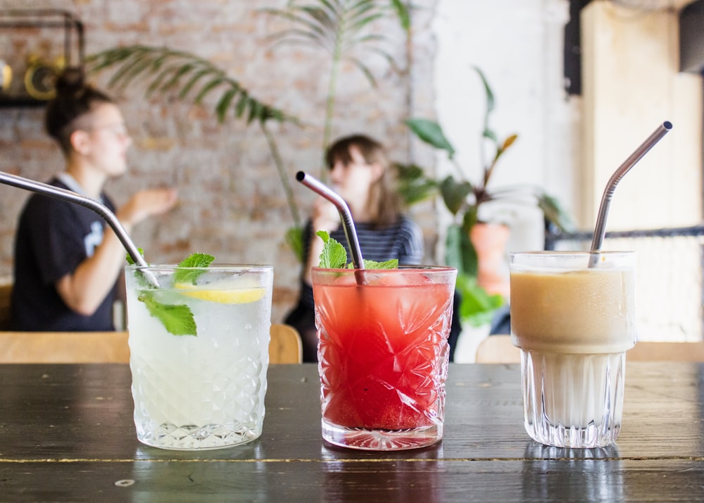 three assorted drinks in glasses with straws