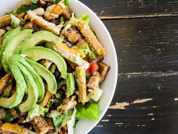 A bright bowl of fresh colorful salad with mixed greens, cherry tomatoes, and avocado slices on a wooden table