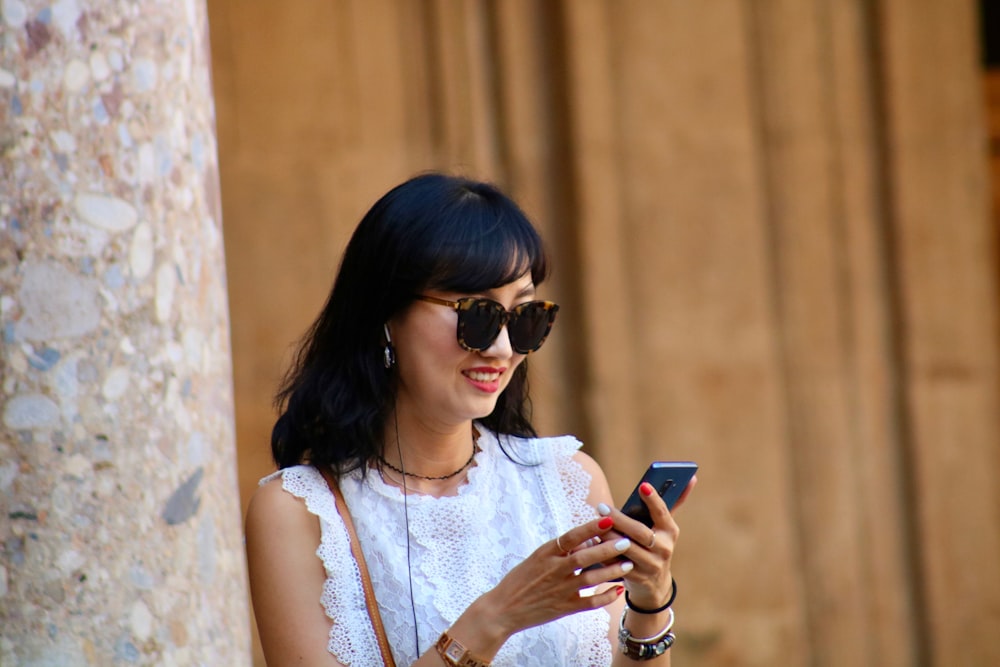 woman in white lace top using smartphone while smiling