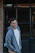 A smiling young man wearing a grey hoodie from crew & co, standing outdoors with a city skyline behind him.