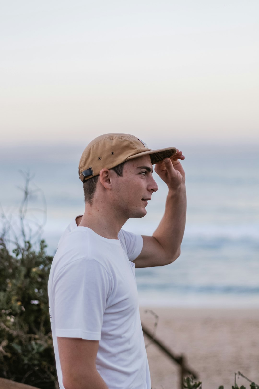 man wearing white crew-neck t-shirt holding his brown fitted cap