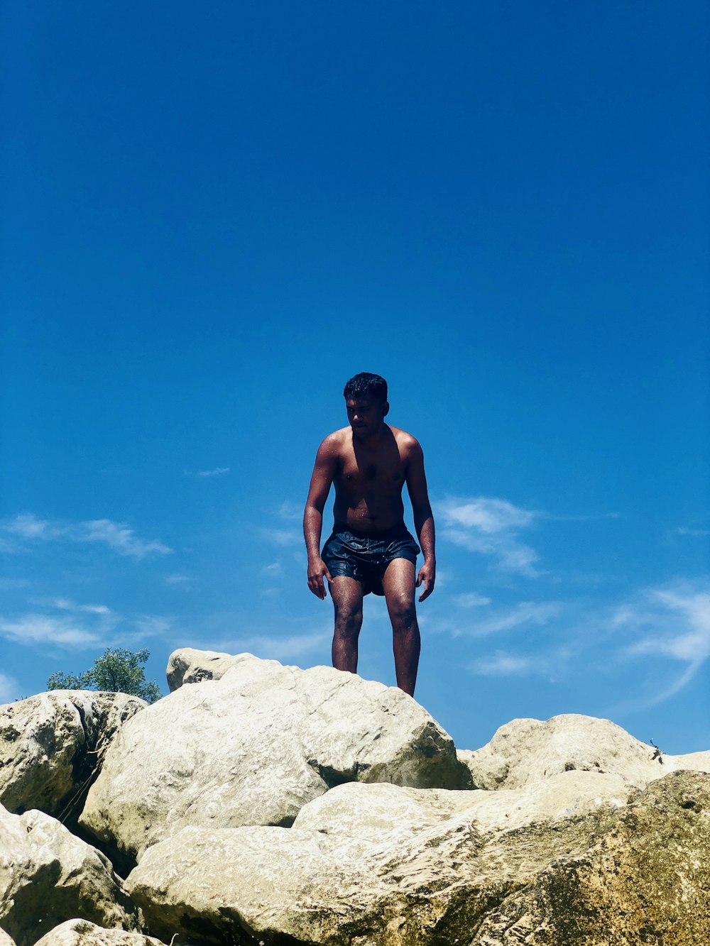 青と白の空の下、岩の上に立つトップレスの男