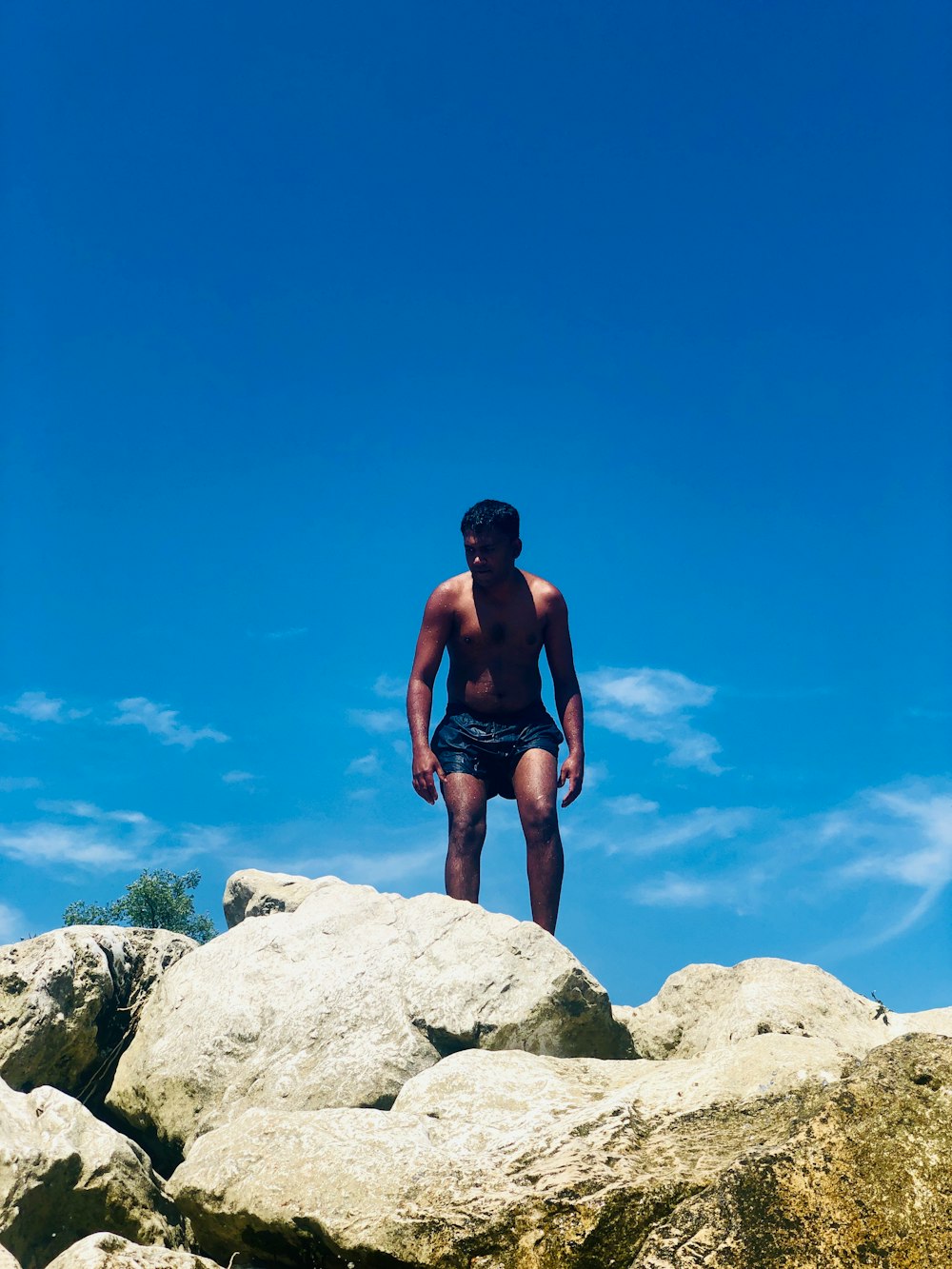 topless man standing on rock under blue and white skies