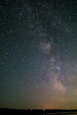 A starry night sky over a quiet countryside, with the Milky Way stretching across.