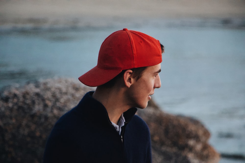 man wearing black jacket and red hat staring on sea