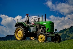 green and black tractor in green field under blue and white skies