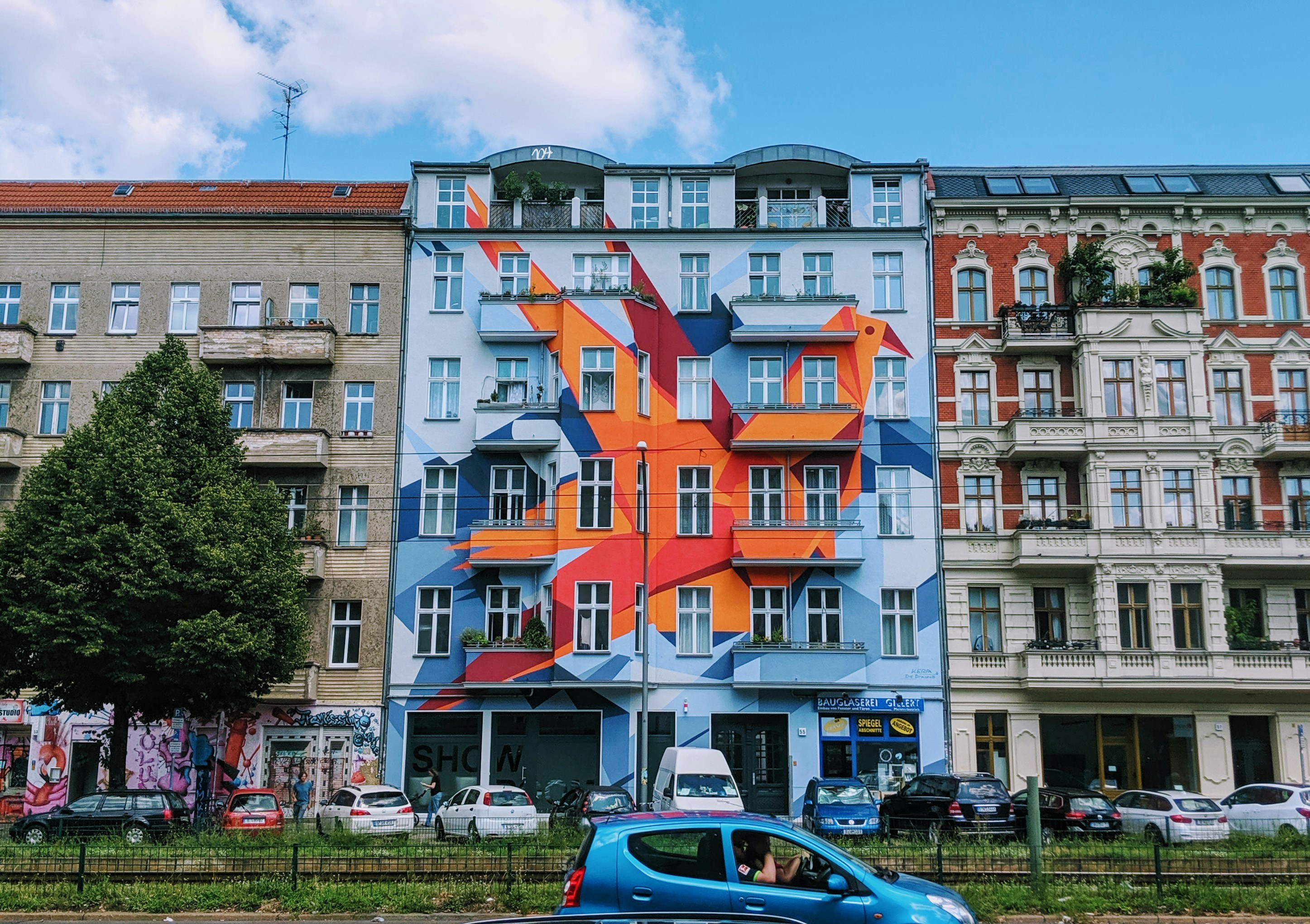 different vehicles parking near multicolored building under blue and white skies, 