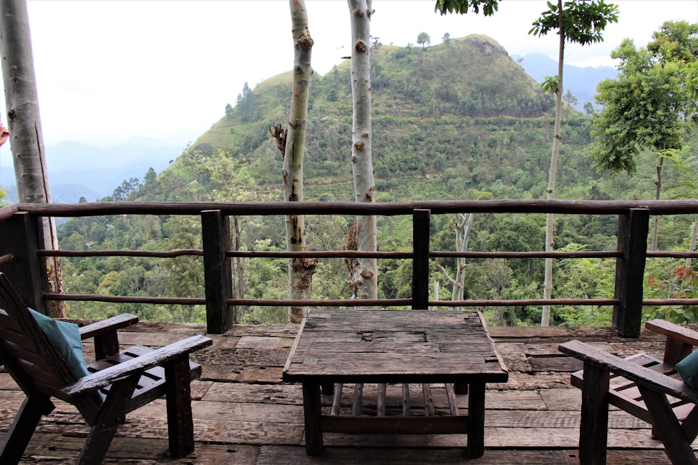 山の景色の前に茶色の木製のパティオテーブルと椅子
