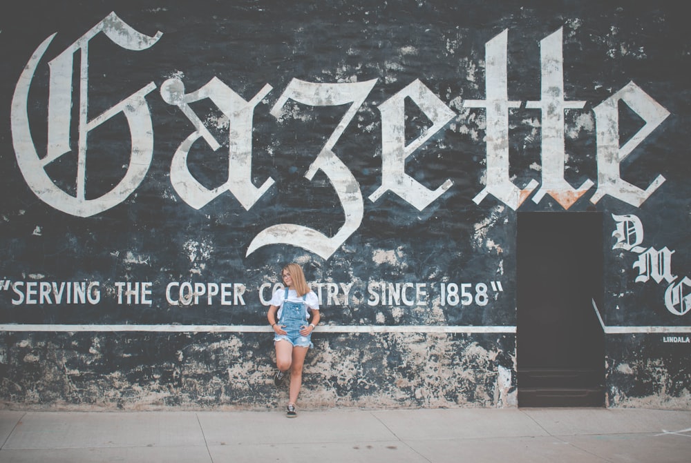 woman standing and leaning on Gazette painted wall during daytime