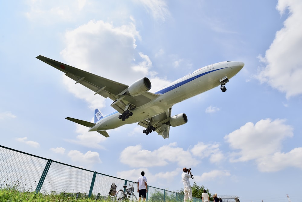 white and blue plane flying above people during daytime