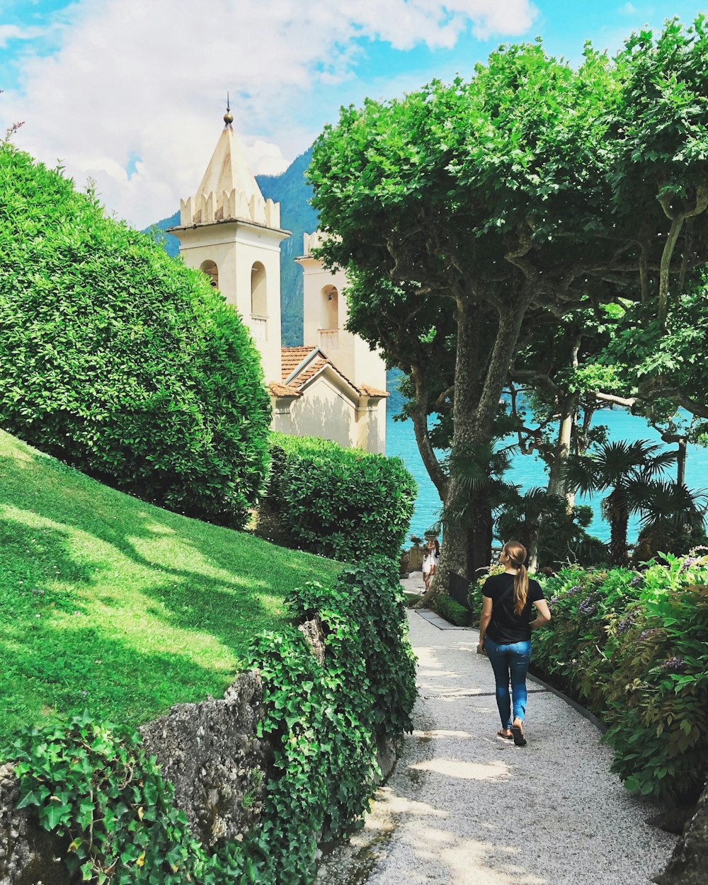 woman walking on pathway in between hedge