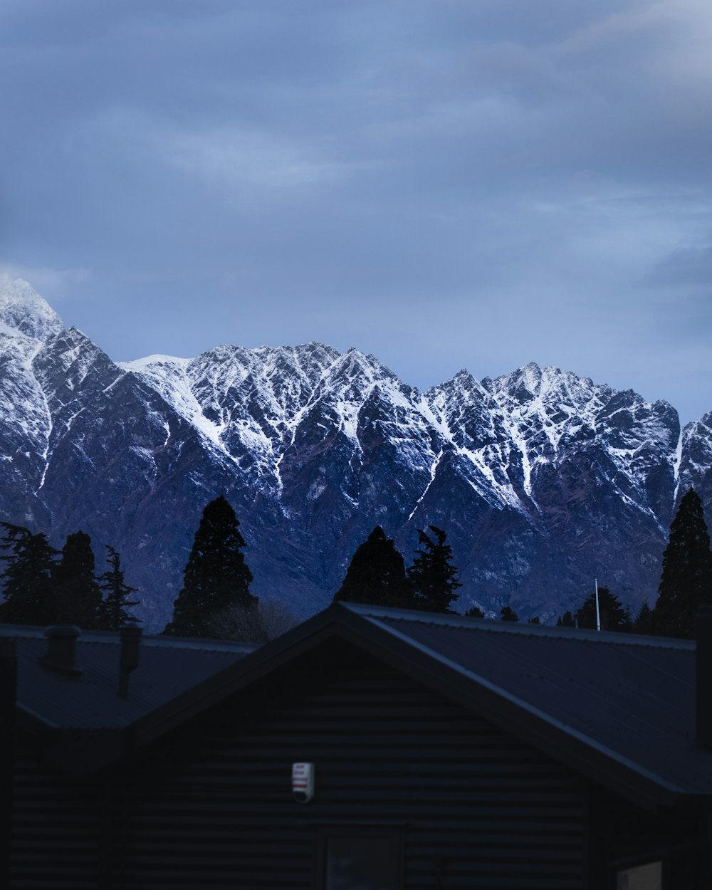 brown house surrounded by trees near snow-capped mountain