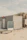 A small wooden beach hut with light-colored panels is situated on a sandy beach. The structure has a frosted glass panel on its porch and a sign with the text 'STRANDLOPER'. In the background, sand dunes topped with grass can be seen under a cloudy sky.