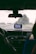 A view from inside a car, looking out through the windshield on a rainy day. A GPS device is mounted on the dashboard, displaying a map. Water droplets are visible on the glass, and there are two people in the front seats, one driver and one passenger.