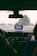 A view from inside a car, looking out through the windshield on a rainy day. A GPS device is mounted on the dashboard, displaying a map. Water droplets are visible on the glass, and there are two people in the front seats, one driver and one passenger.