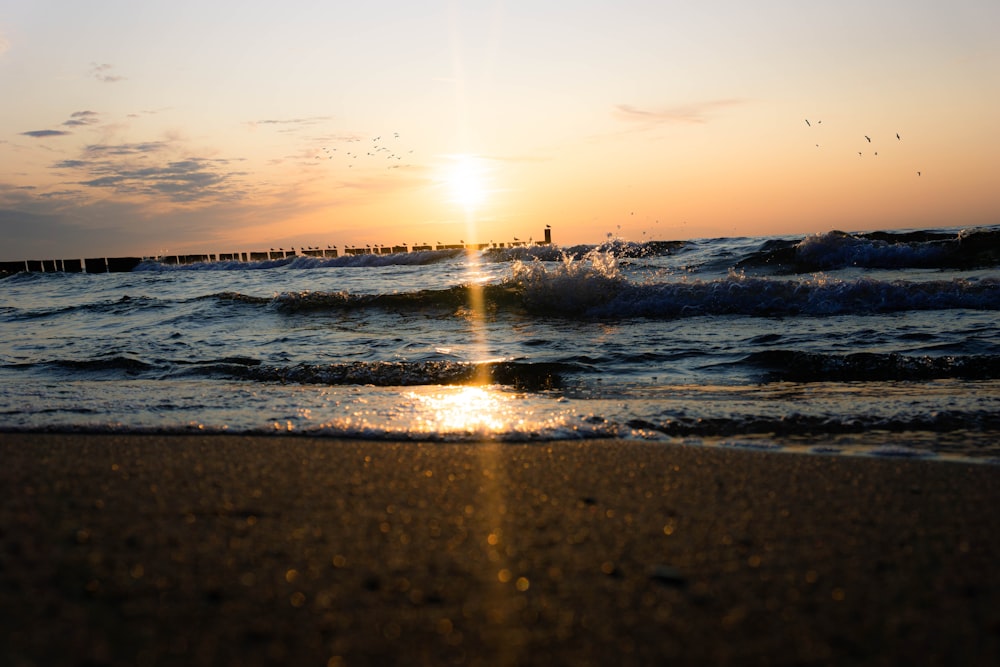 the sun is setting over the water at the beach