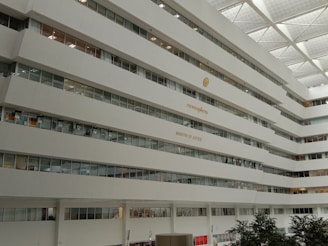 A large multi-story building interior with rows of windows and a sign indicating 'Ministry of Justice'. The architecture is modern with a white color scheme, and some greenery is visible at the bottom of the image.